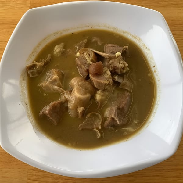 A white square bowl filled with a hearty African soup containing various cuts of meat.