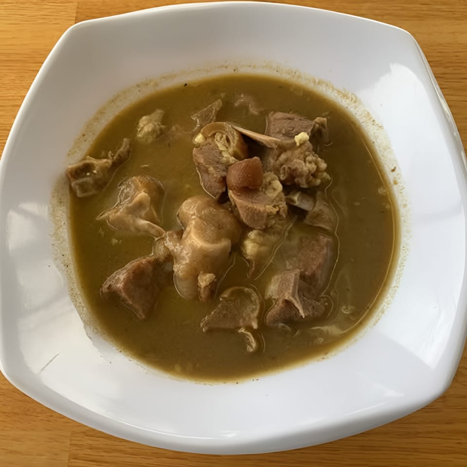 A white square bowl filled with a hearty African soup containing various cuts of meat.