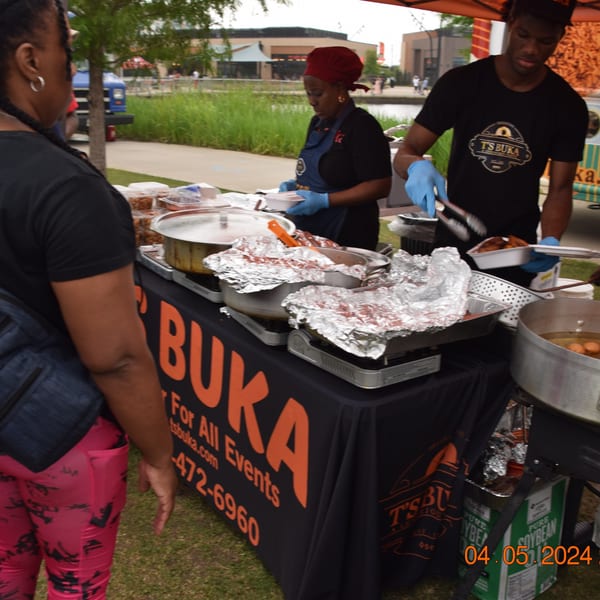 T's Buka staff serving African cuisine from a food stall outdoors to a customer.