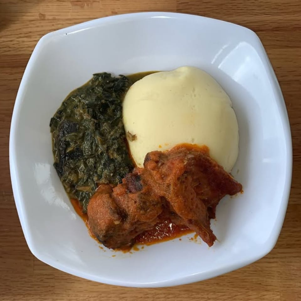 T's Buka African dish with fufu, green stew, and meat in red sauce on a white plate.