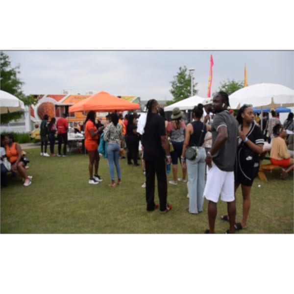 People gather on a grassy field with white and orange tents, enjoying an outdoor event.