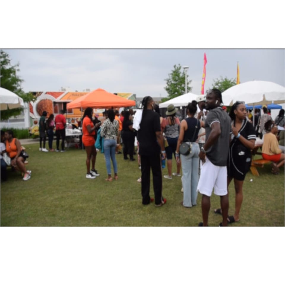 People gather on a grassy field with white and orange tents, enjoying an outdoor event.